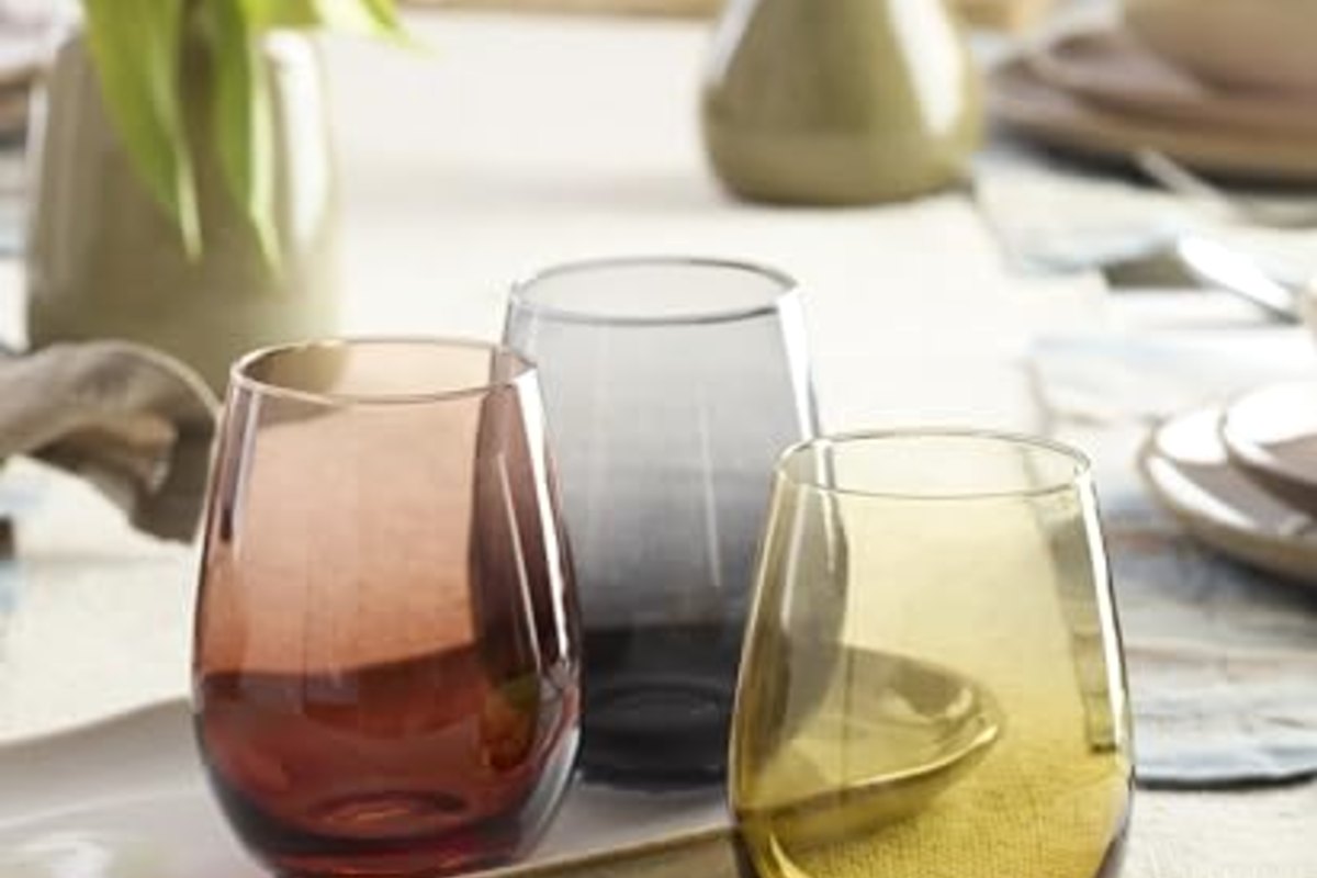 Coloured stemless glasses on a linen runner beside a set place