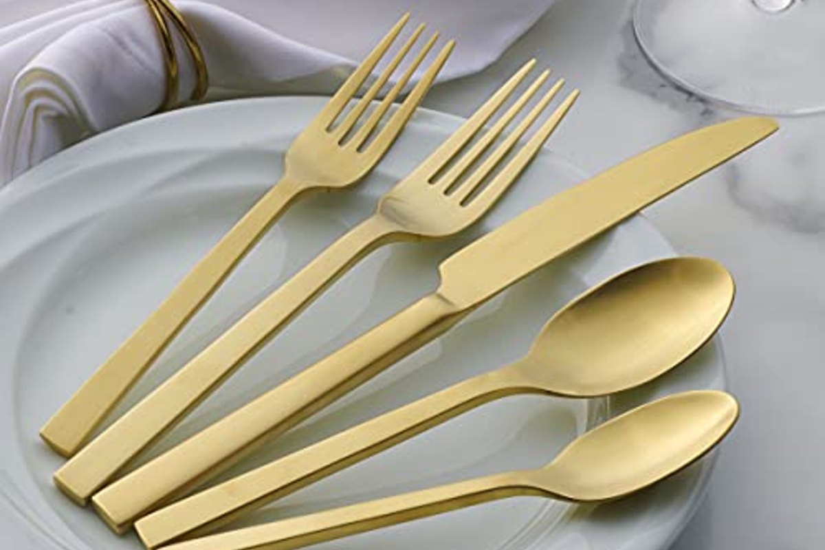 Champagne-toned forks and spoons laid across a white plate with a lilac napkin ring