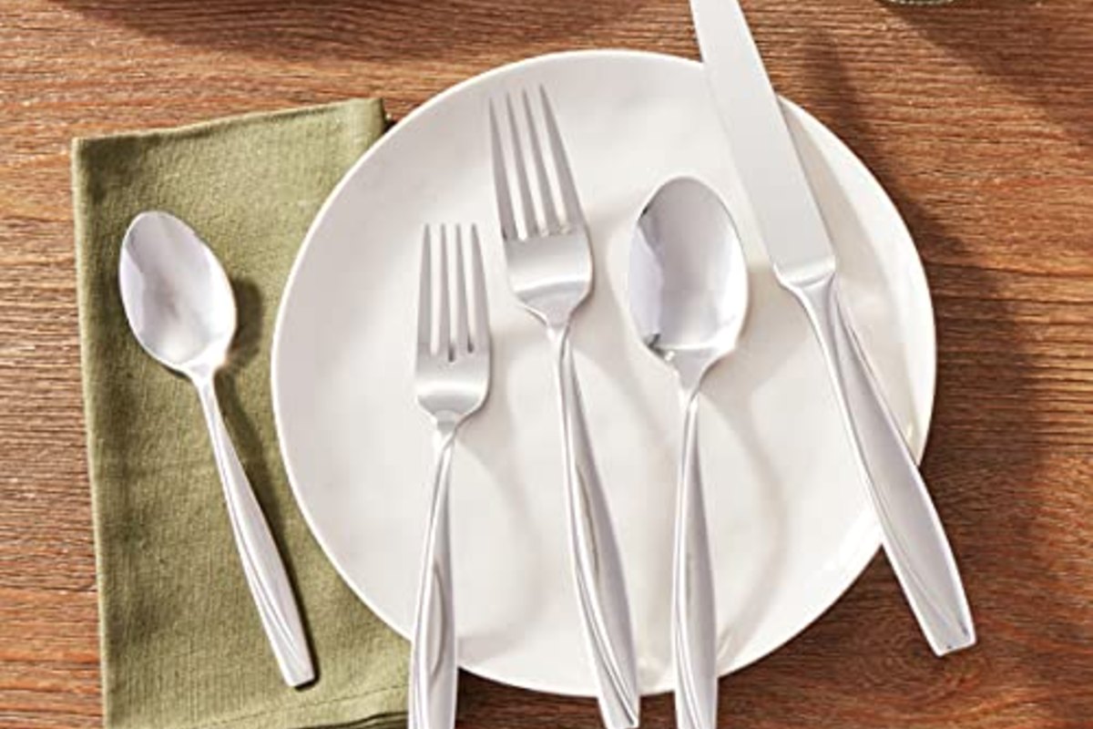 A single place setting laid on a warm wood table, fork and spoons resting on a folded green napkin beside a white plate