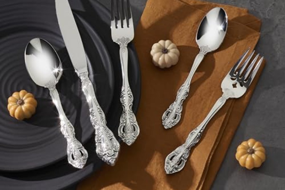 Ornate flatware arranged on a dark slate plate and a folded ochre napkin